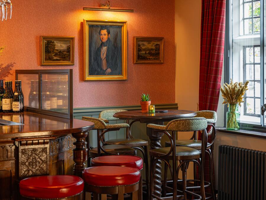 A bar area with wooden stools, a bar counter, and framed artwork on the wall.