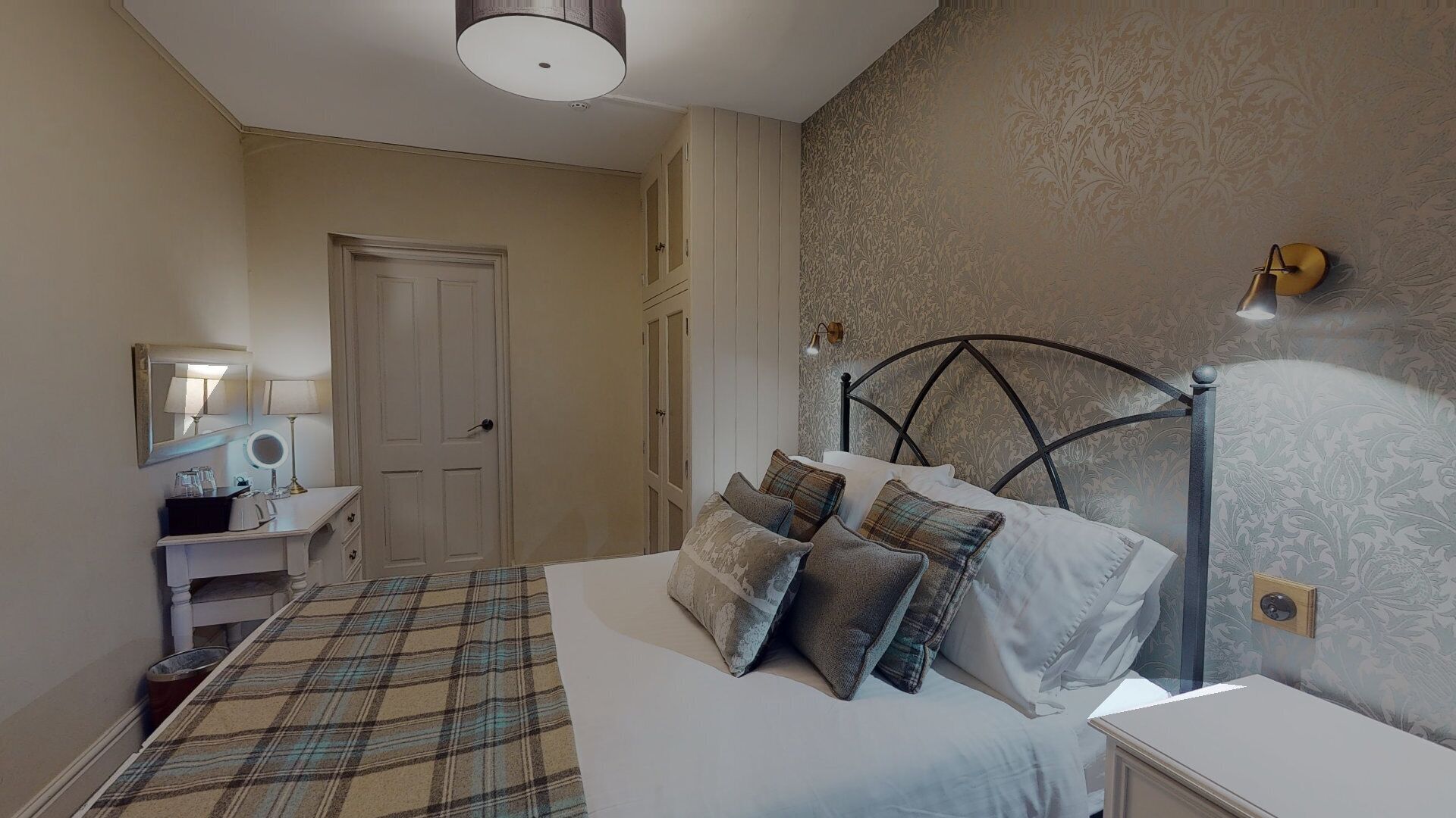 A bedroom with a bed, bedside table, lamp, and a door leading to another room.