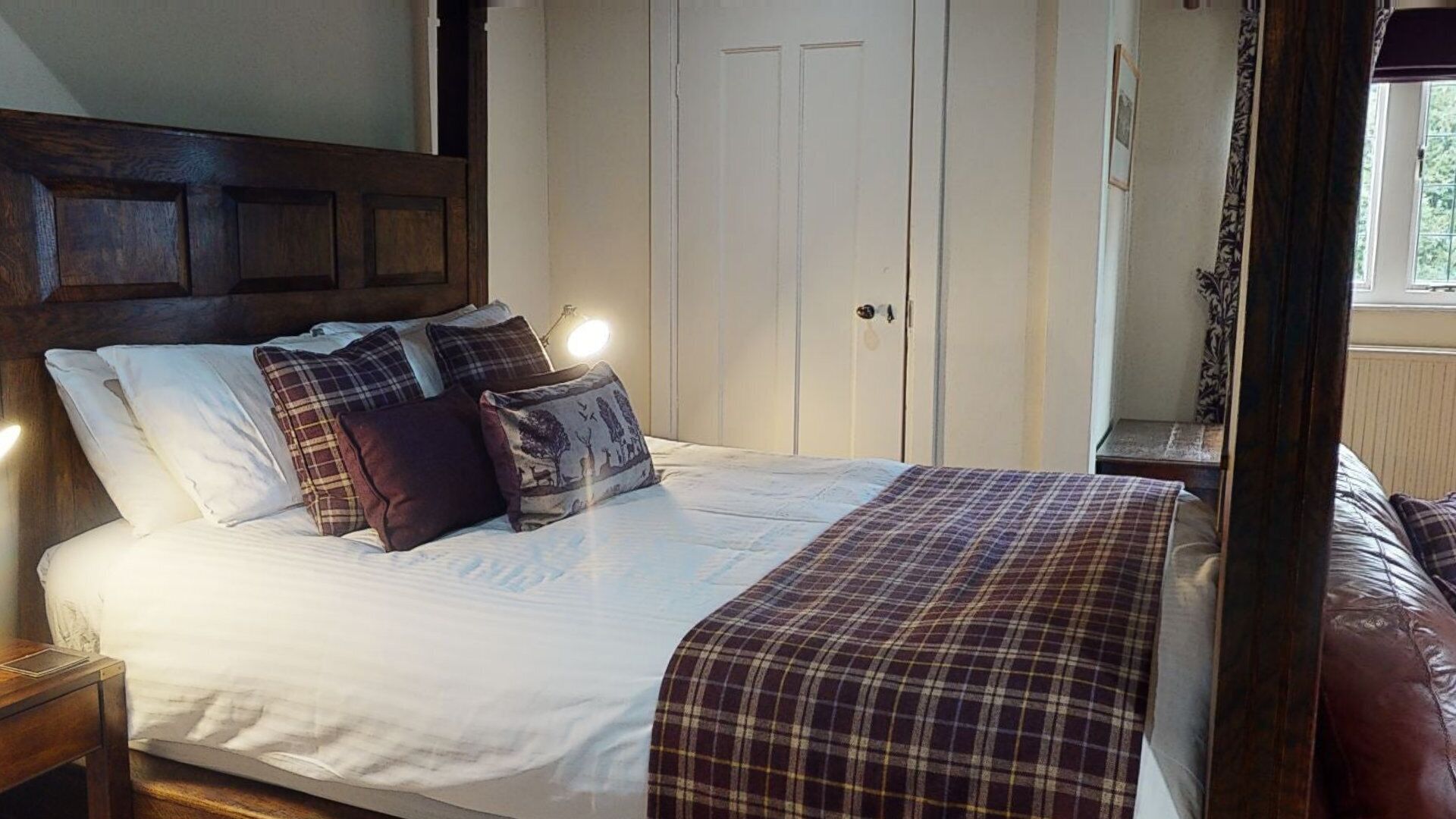 Un dormitorio con una cama grande, cabecera de madera, paredes blancas, un armario y una ventana con cortinas.