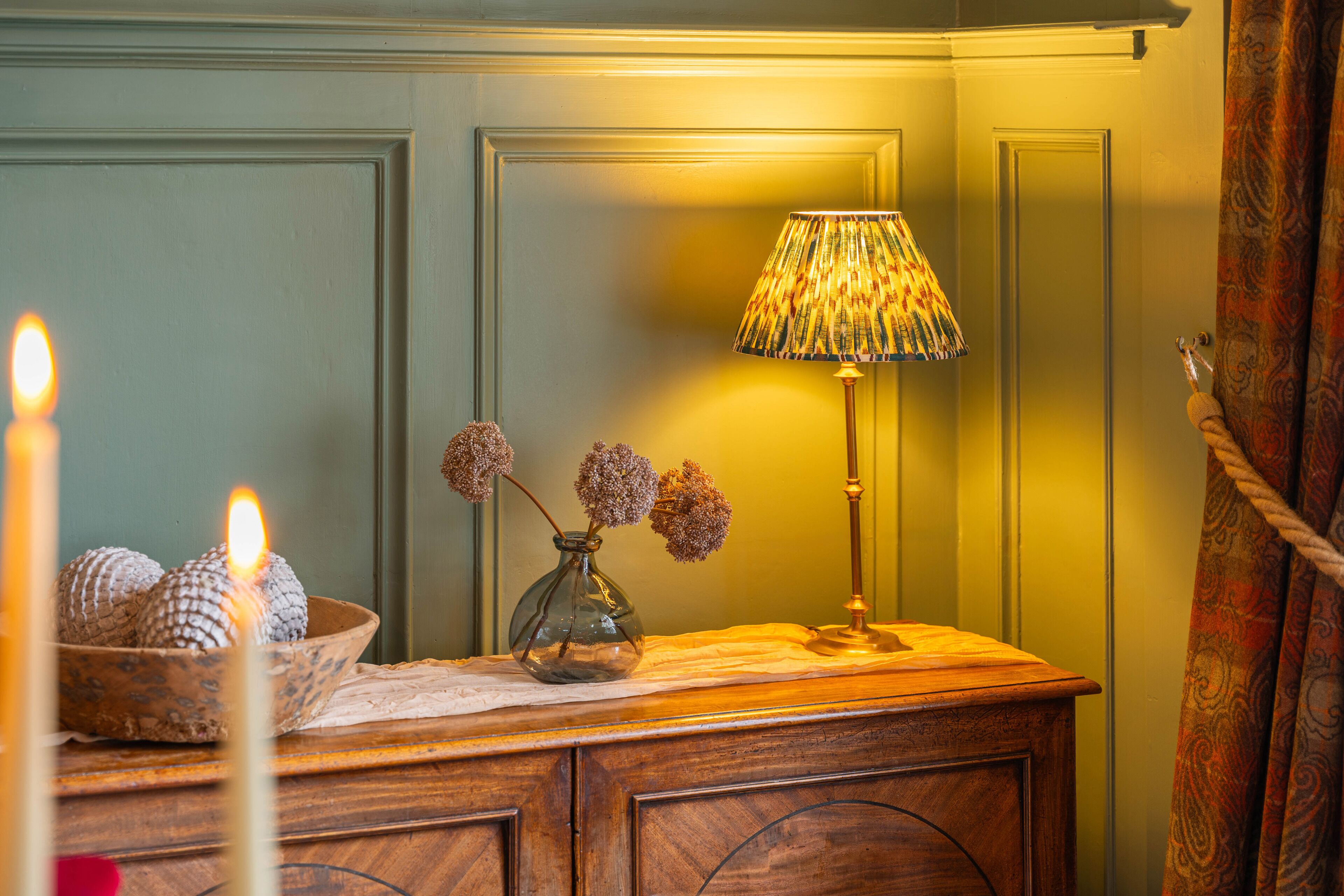 Ein Holzsideboard mit einer Vase getrockneter Blumen und einer Kerze.