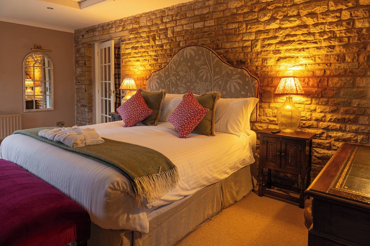 A neatly made bed with pillows and a blanket, a stone wall, and two lamps on nightstands.