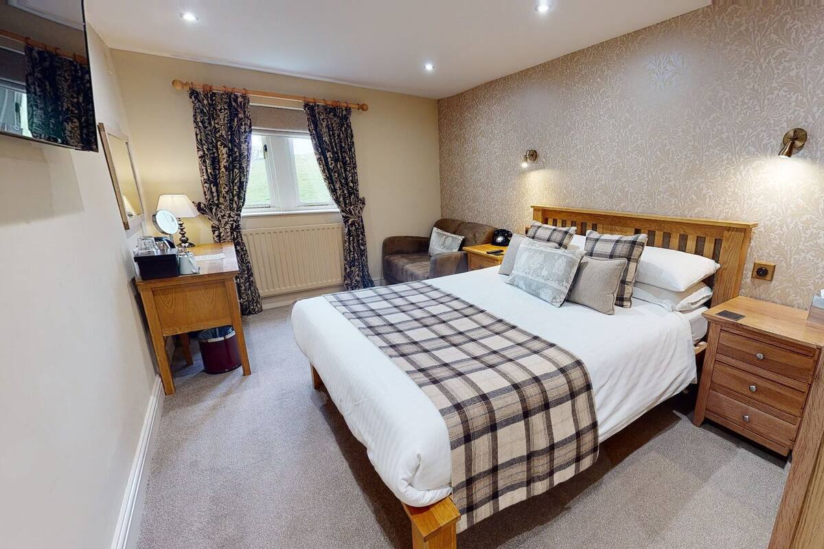 A bedroom with a bed, bedside tables, a nightstand, a mirror, a window with curtains, and a wall-mounted light fixture.
