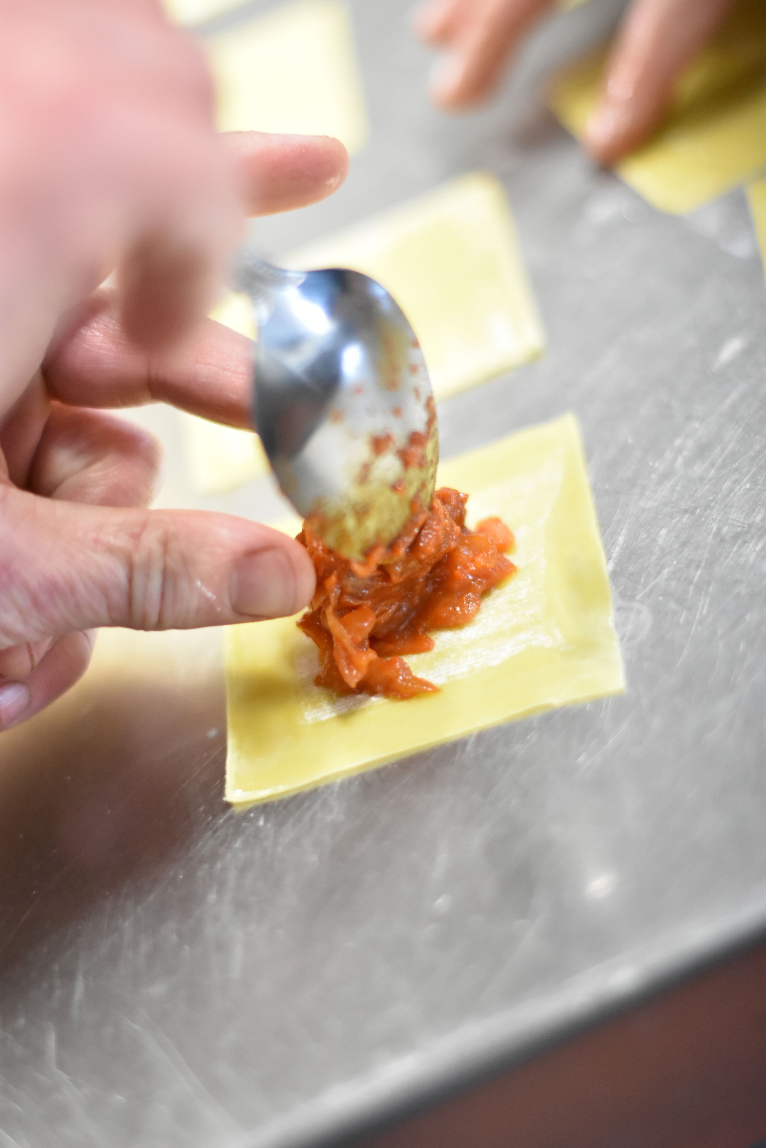 A hand spreading sauce on a ravioli.
