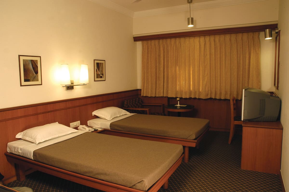A hotel room with two single beds, a television, a small table, and a lamp.