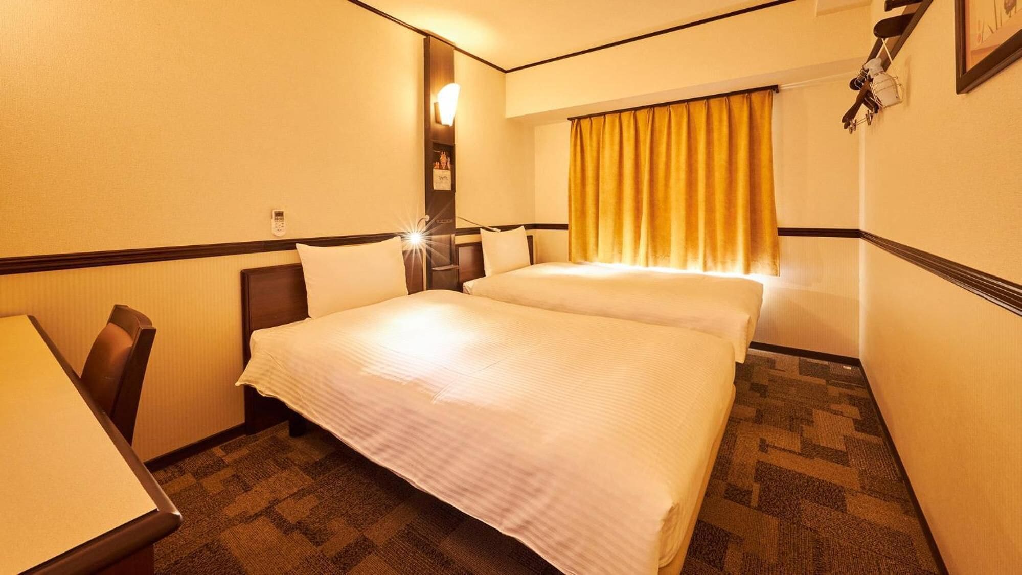 A hotel room with two beds, a desk, a telephone, and a window with yellow curtains.