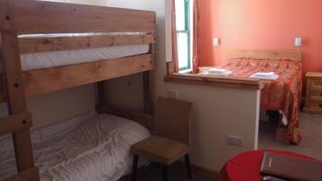 Habitación con literas, una ventana, una silla, una mesita de noche y una mesa roja con un control remoto.