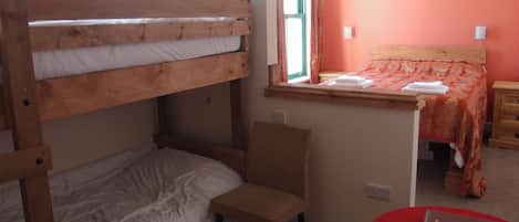 Habitación con literas, una ventana, una silla, una mesita de noche y una mesa roja con un control remoto.