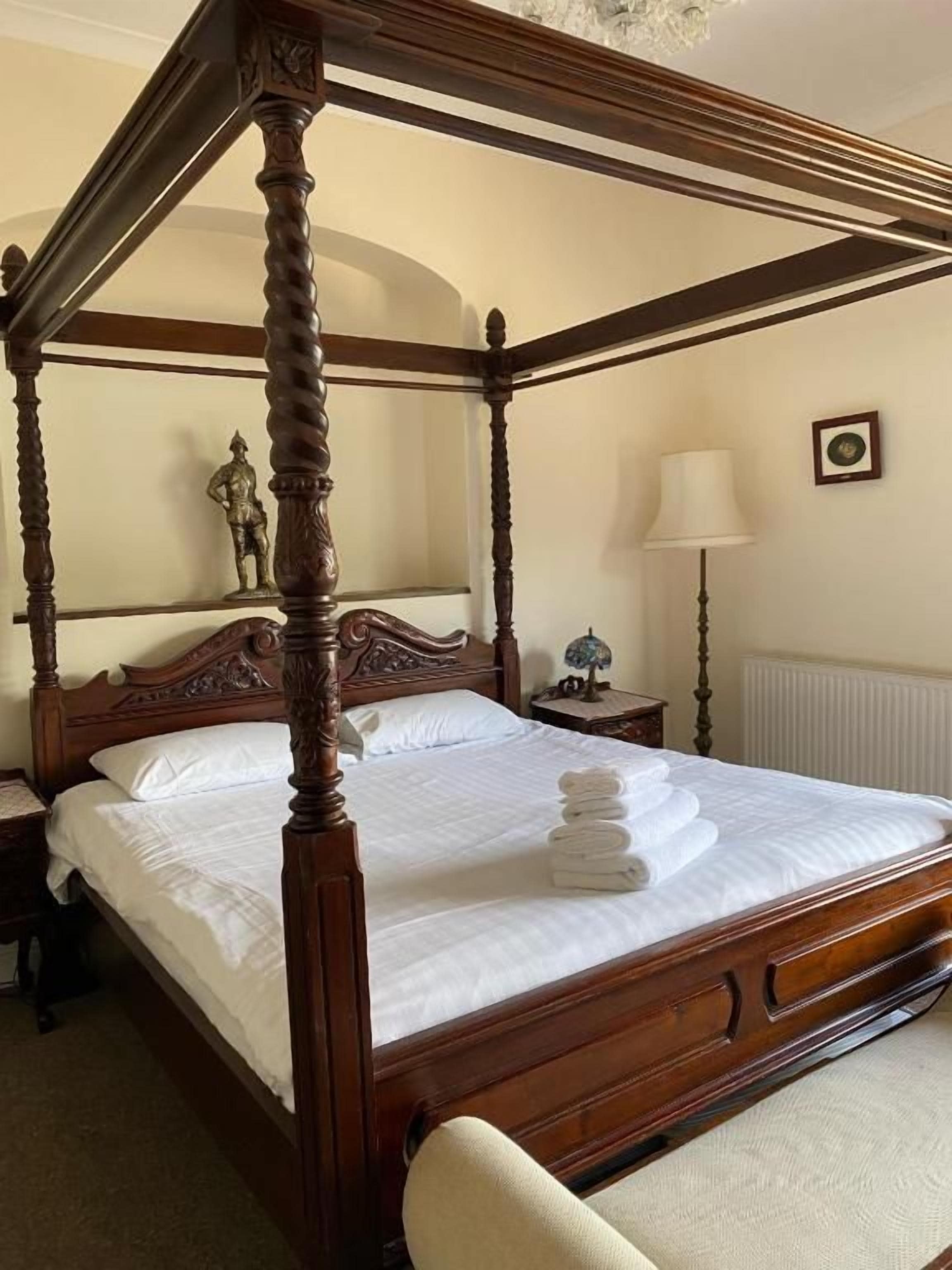 A four-poster bed with a wooden frame, a white bedspread, and neatly folded towels on the bed.