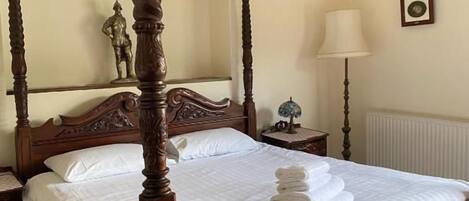 A four-poster bed with a wooden frame, a white bedspread, and neatly folded towels on the bed.
