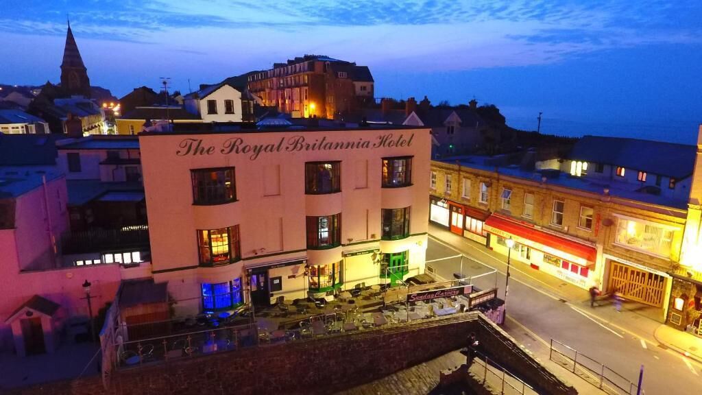 The Royal Britannia Hotel with a prominent sign, a courtyard with outdoor seating, and a view of the surrounding townscape.