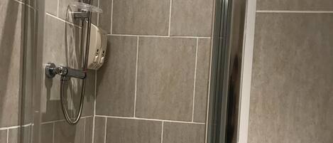 Aseo con mampara de vidrio, cabezal de ducha de mano y panel de control en la pared.