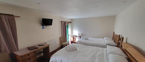 A hotel room with two wooden beds, a desk with a chair, a television, and a window with curtains.