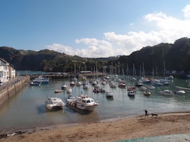 Un puerto deportivo con varias embarcaciones amarradas, una playa de arena y un paisaje montañoso al fondo.