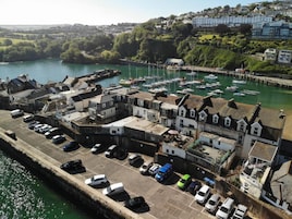 Un pueblo costero con un puerto deportivo, coches aparcados y edificios de arquitectura tradicional.