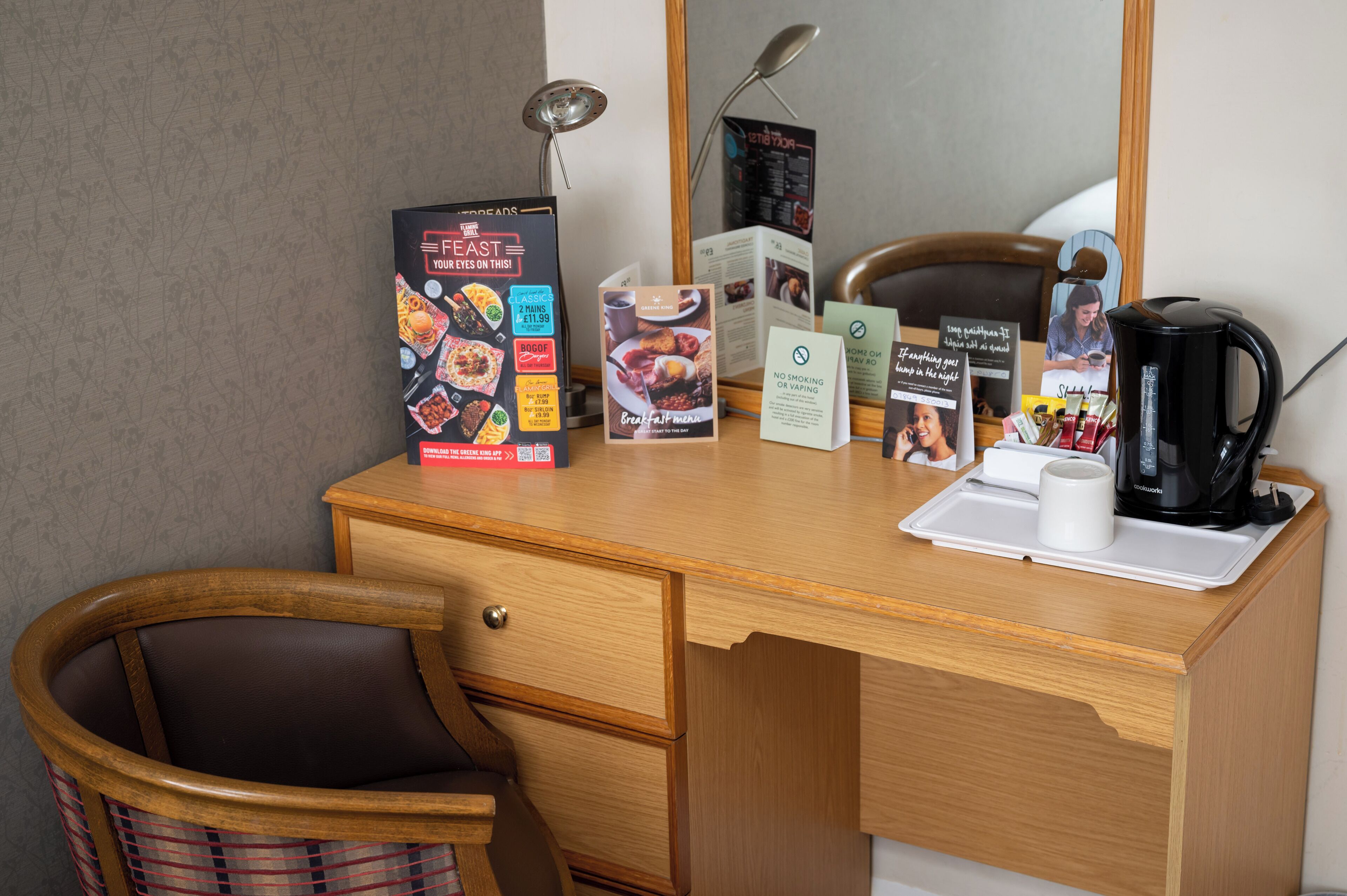 A wooden desk with a coffee maker, a tray with a cup, a menu, and a sign about no smoking or vaping.
