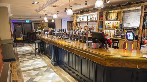 A bar area with a wooden counter, multiple taps, and a digital payment terminal. - Old Grey Mare Hotel by Greene King Inns (Hull)