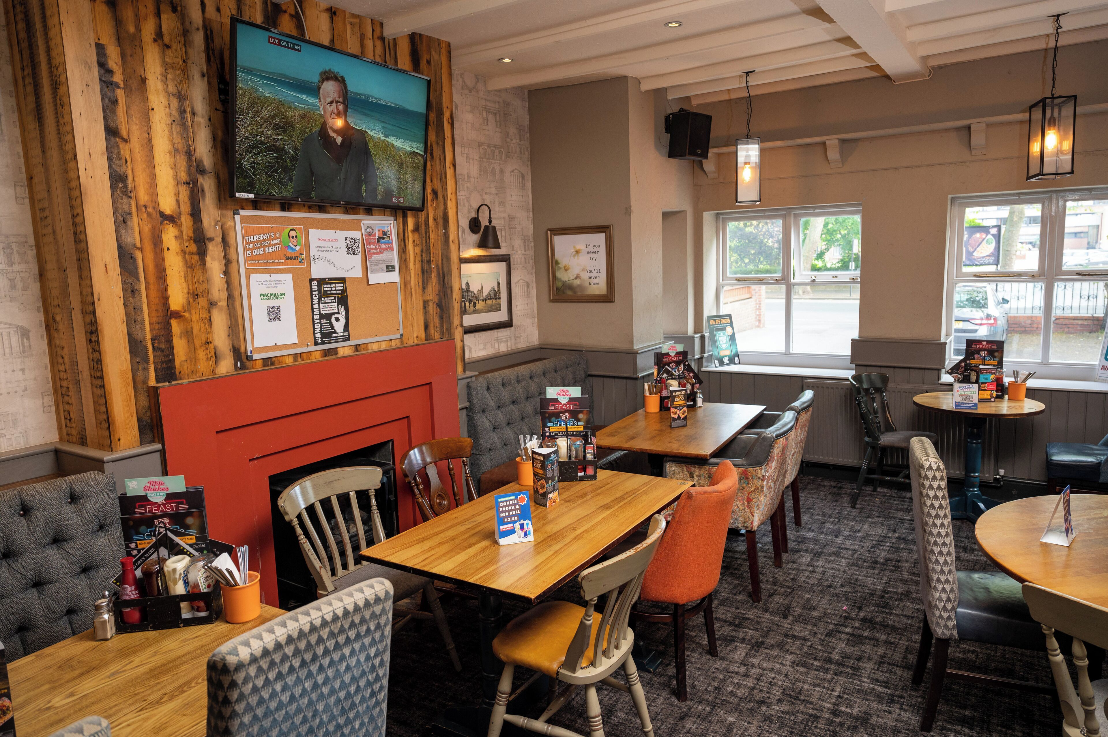 A restaurant with wooden walls, multiple tables, and chairs. There is a TV mounted on the wall and a fireplace.
