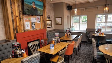 A restaurant with wooden walls, multiple tables, and chairs. There is a TV mounted on the wall and a fireplace.