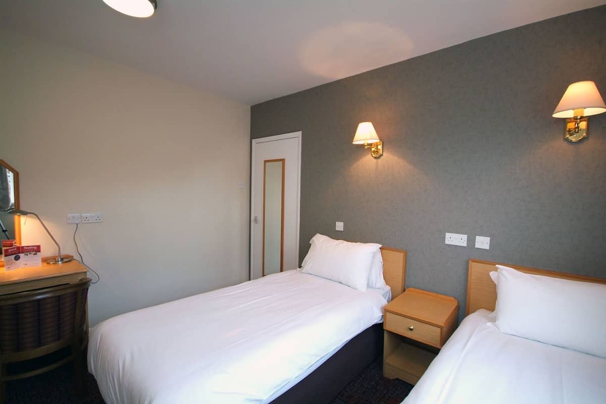 Habitación de hotel con dos camas, lámparas de noche, cómoda y espejo.