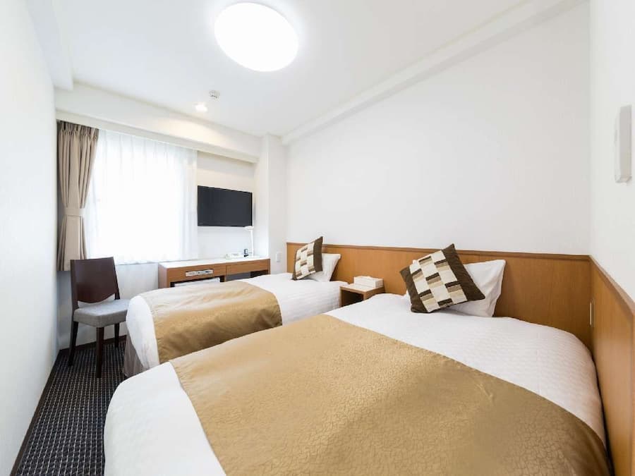 Habitación de hotel con dos camas, un escritorio, una silla, un televisor y una ventana con cortinas.