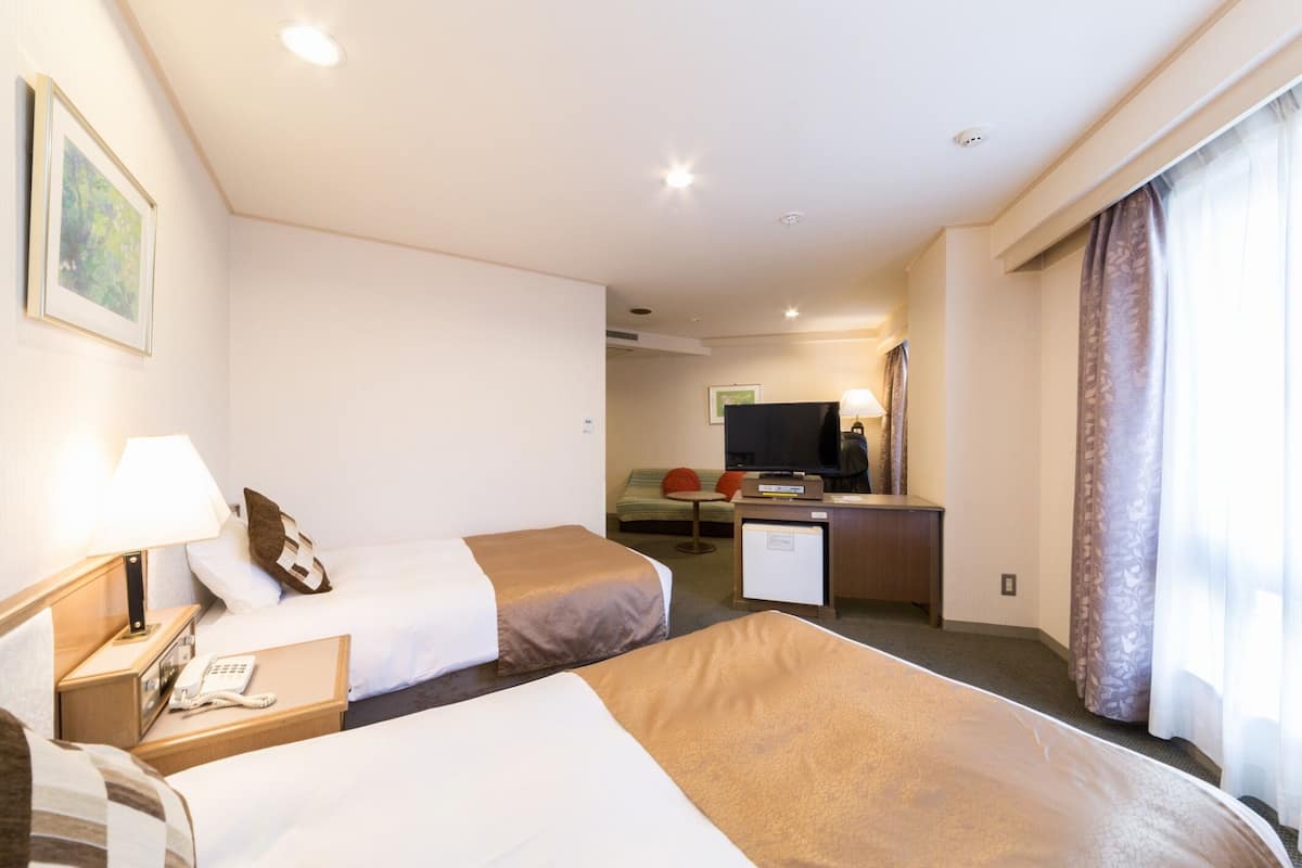 Habitación de hotel con dos camas, un escritorio, un televisor y un refrigerador pequeño.