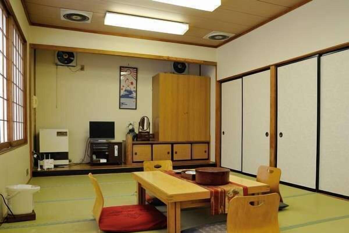A traditional Japanese room with tatami flooring, a low wooden table, a red cushion, a wooden cabinet, and sliding doors.
