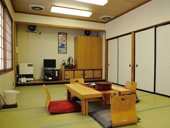 A traditional Japanese room with tatami flooring, a low wooden table, a red cushion, a wooden cabinet, and sliding doors.