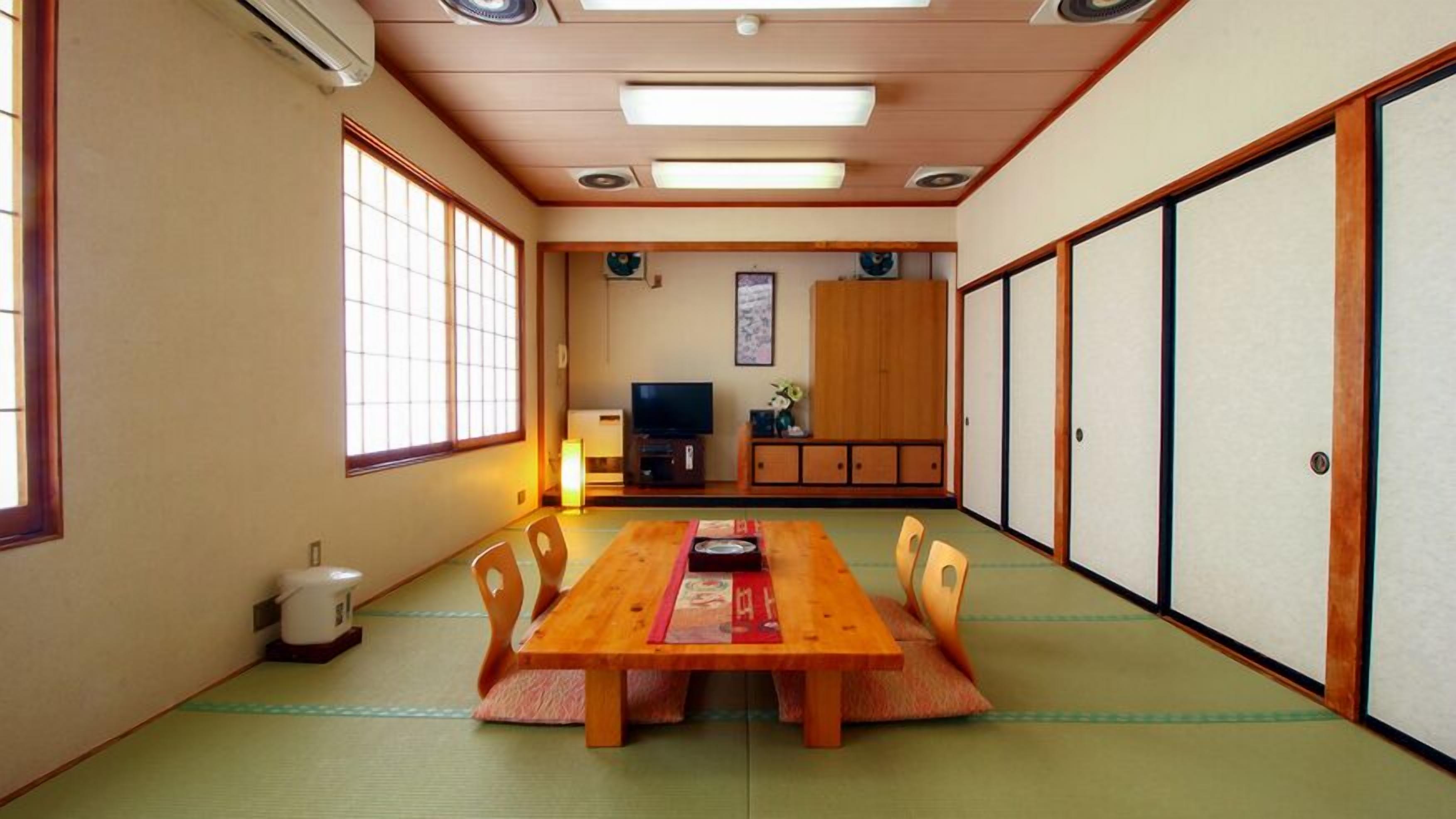 Une pièce de style japonais traditionnel, avec un sol recouvert de tatamis, une table en bois, un téléviseur et des portes coulissantes.