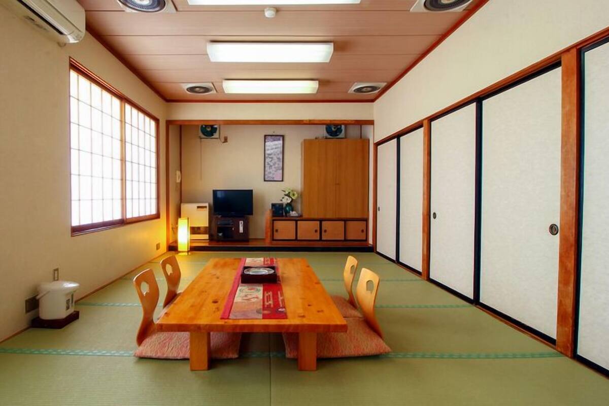 A traditional Japanese room with tatami flooring, a wooden table, a television, and sliding doors.