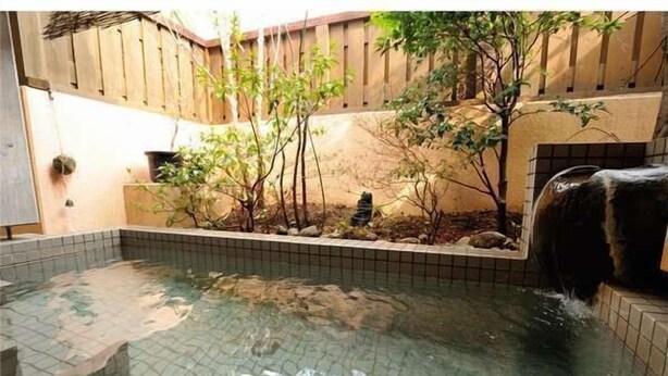 A small outdoor hot tub area with tiled flooring, surrounded by a wooden fence and some greenery. - Oyado Ichifuji (Nikko)