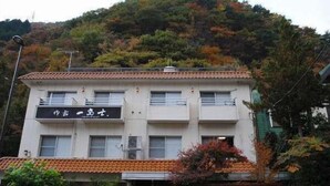 A multi-story building with a signboard, surrounded by trees and a hilly landscape. - Oyado Ichifuji (Nikko)