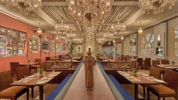 A restaurant with a long central table, multiple chandeliers, and wall-mounted decor.