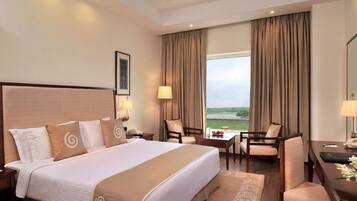 A hotel room with a large bed, two bedside tables, a desk with a chair, a TV, and a window with curtains.