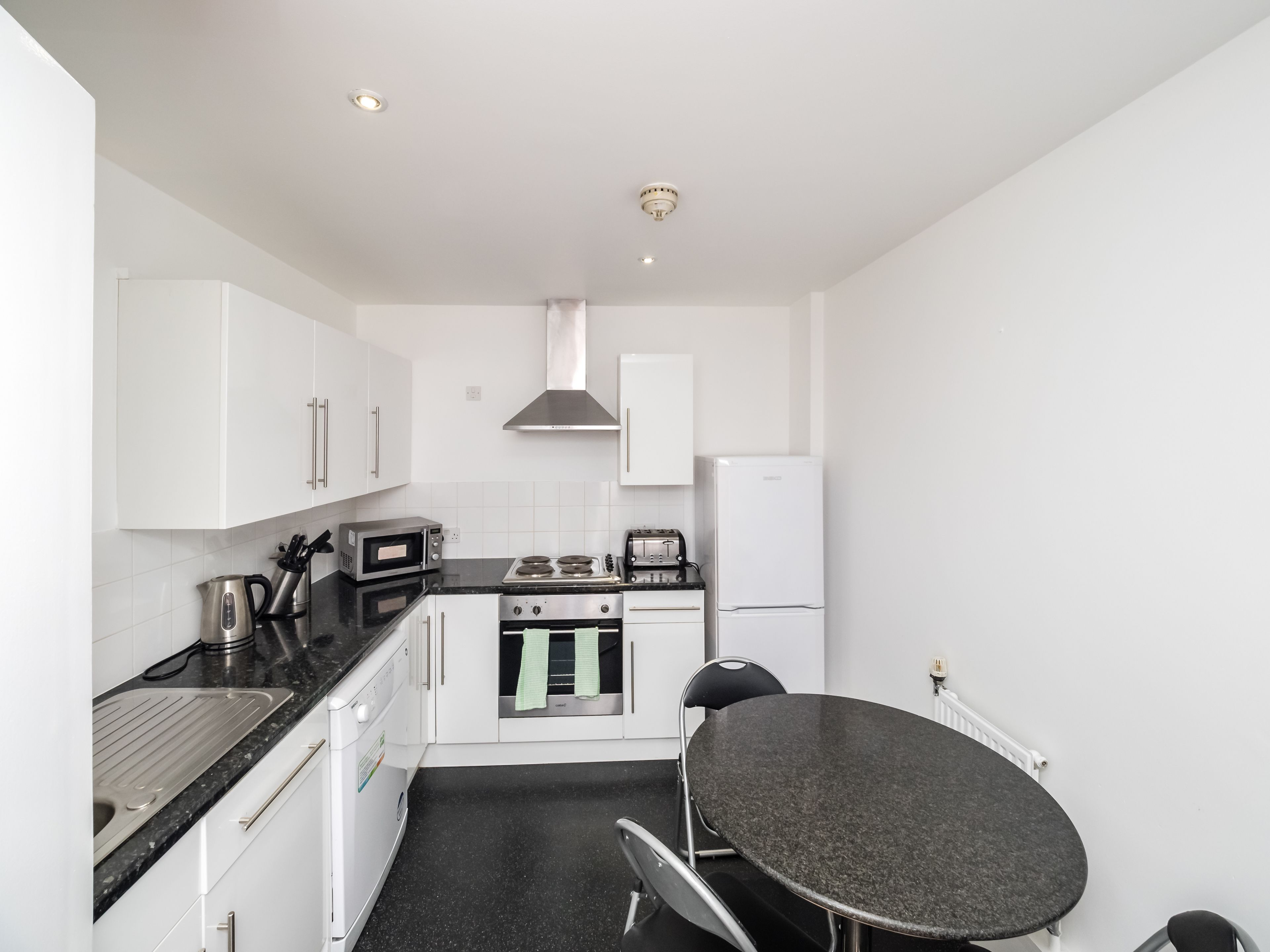 A compact kitchen with white cabinets, a stove, a microwave, a toaster, and a refrigerator.