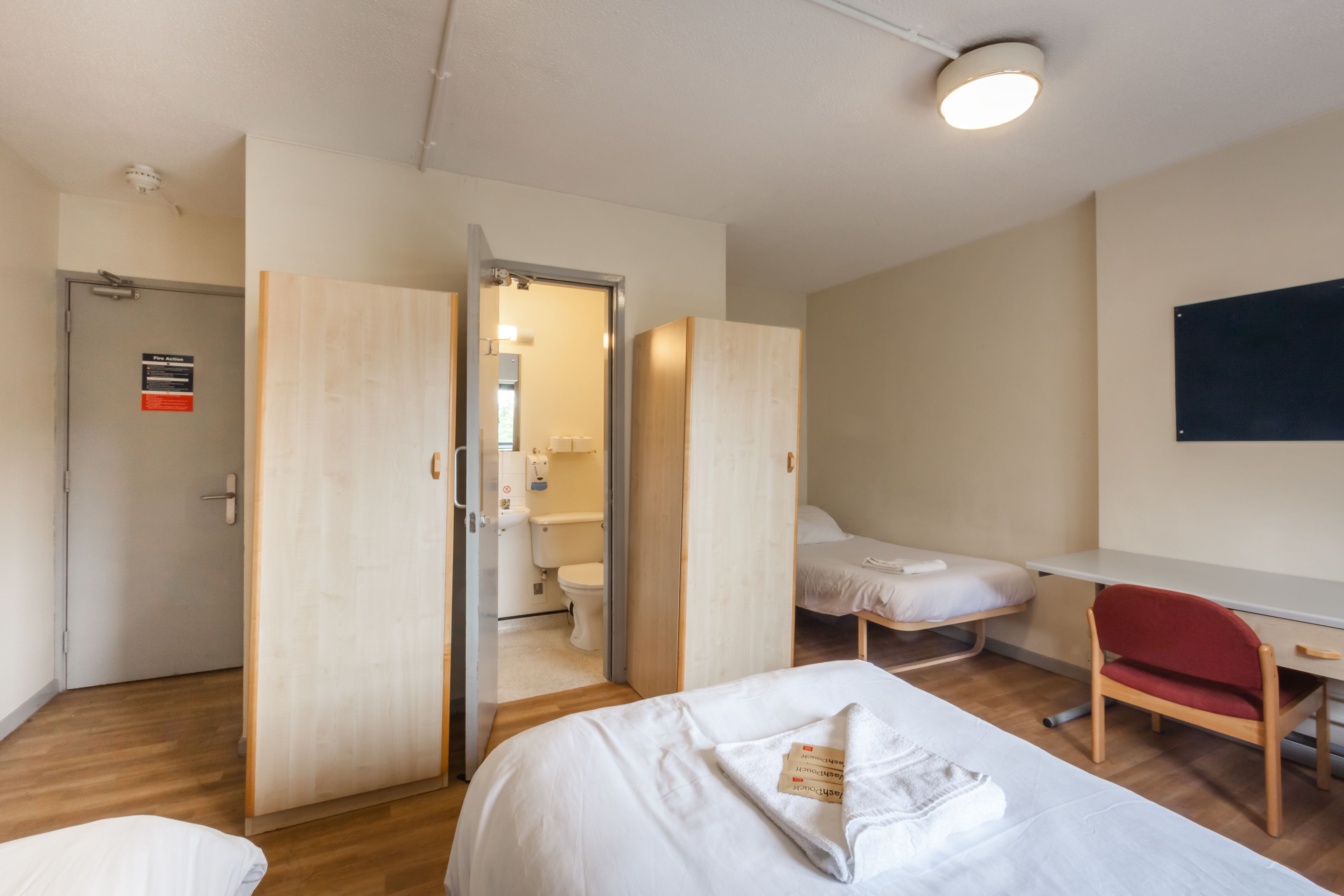 A hotel room with a bed, a desk, a chair, and a bathroom visible through an open door.