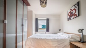 Quarto moderno com cama, mesa de cabeceira, luminária e um quadro na parede.