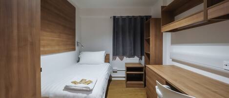 Una habitación de hotel pequeña con una cama, un escritorio y una silla.