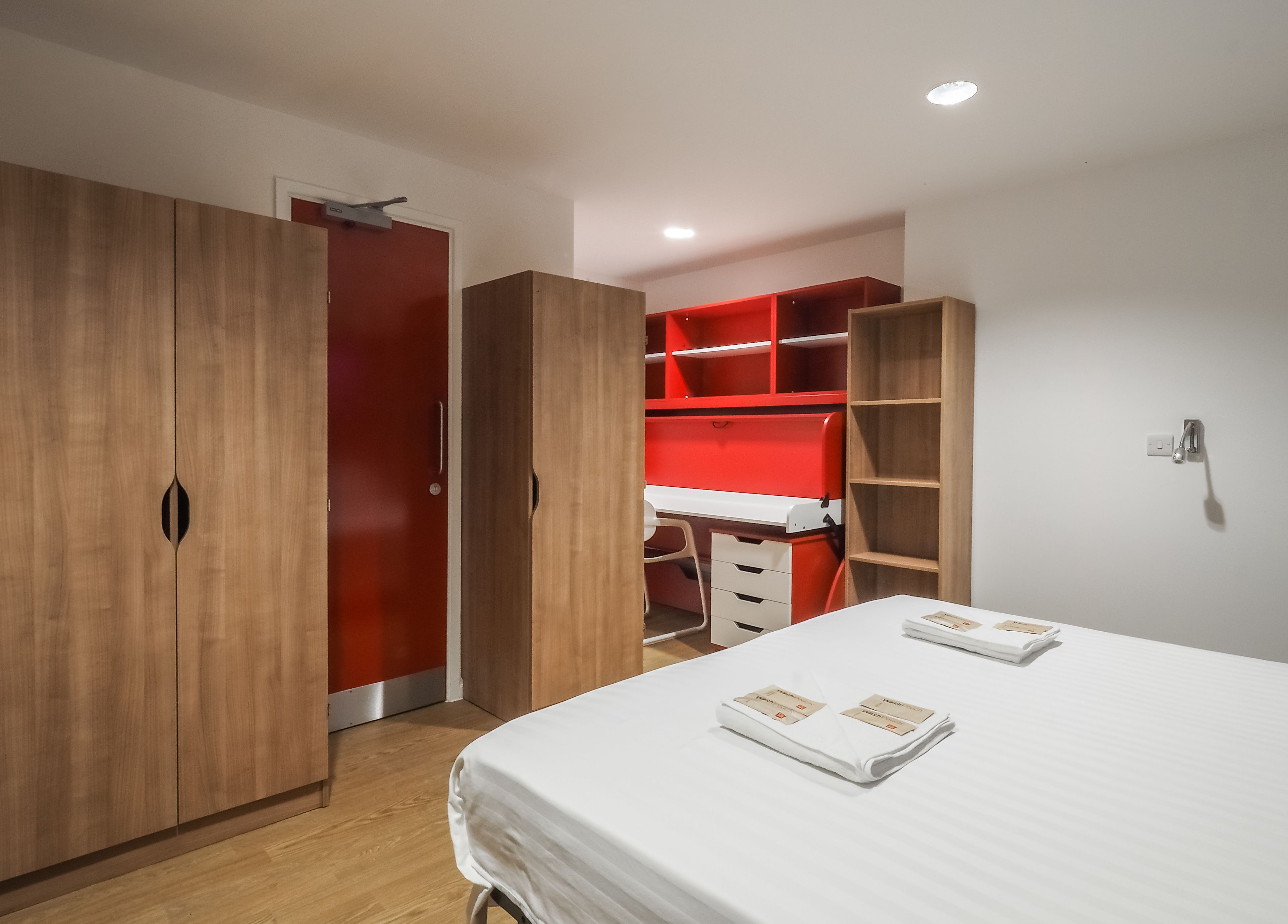 Een slaapkamer met een bed, een houten garderobe en een rode schapunit.