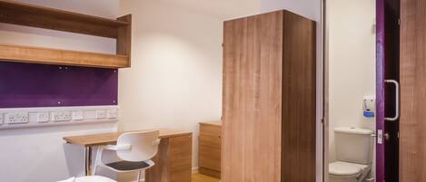 A compact hotel room with a bed, a desk, a chair, a wardrobe, and a bathroom.