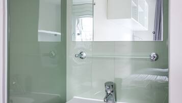 Un baño con lavamanos blanco, espejo y cabina de ducha de vidrio.