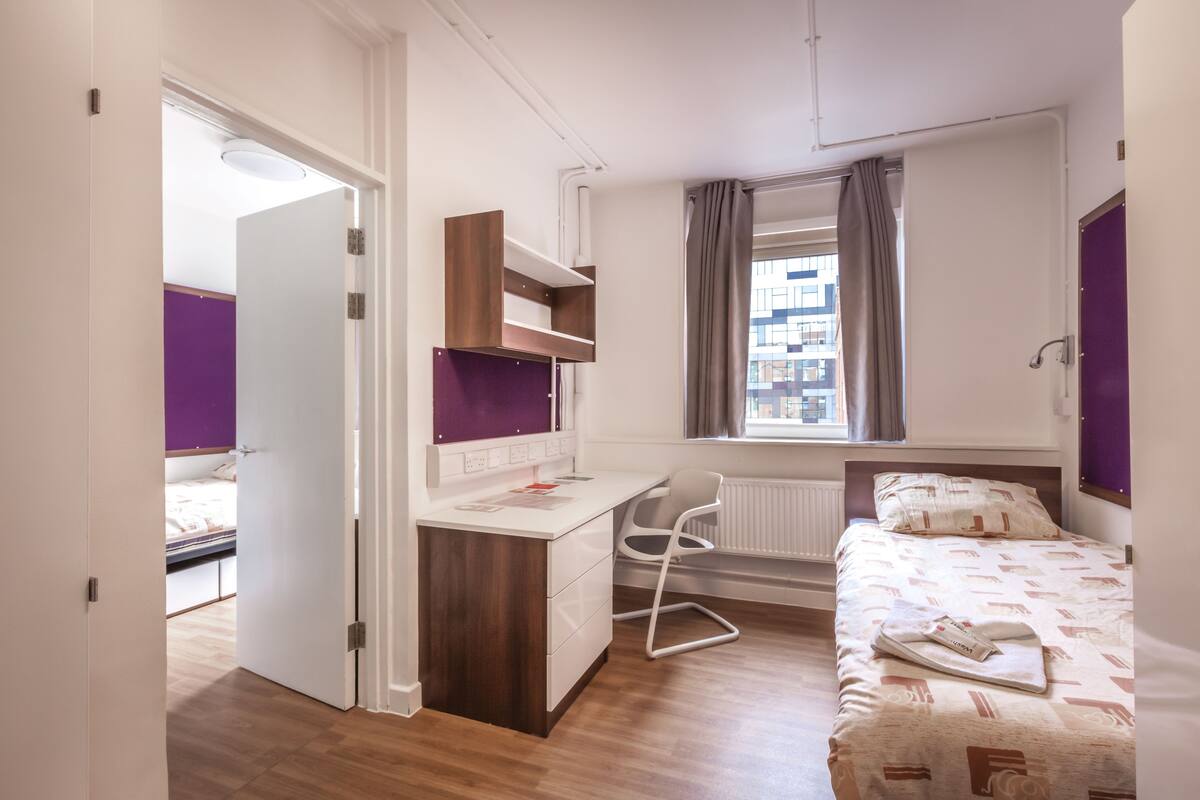 Un dormitorio moderno con cama, escritorio, silla y ventana con cortinas.