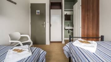 A hotel room with two beds, a wooden wardrobe, a bathroom with a mirror, and a white chair.
