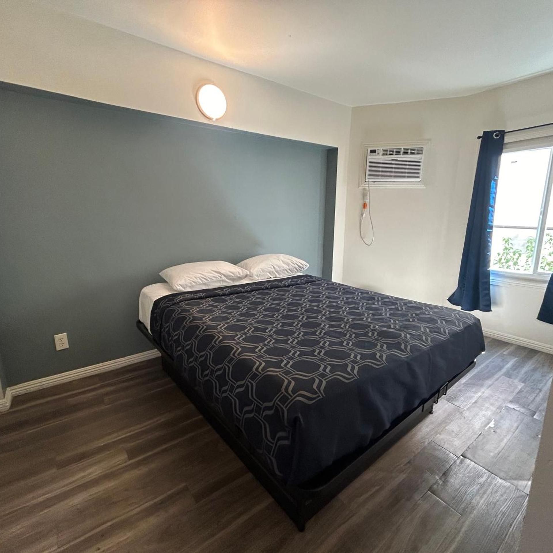 A bedroom with a bed, a wall-mounted air conditioner, and a window with curtains.
