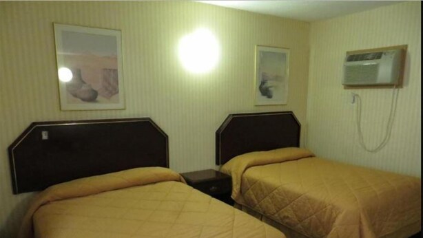 A hotel room with two single beds, a nightstand, a wall-mounted air conditioner, and framed pictures on the wall. - Budget Inn Hollywood (Hollywood)