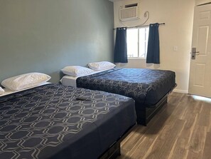 A room with two beds, each with patterned bedding, a window with curtains, and an air conditioning unit on the wall. - Budget Inn Hollywood (Hollywood)
