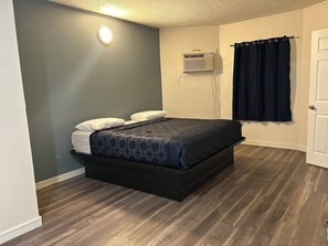 A single bed with a dark headboard and footboard, a wall-mounted air conditioner, and a dark curtain on a window. - Budget Inn Hollywood (Hollywood)