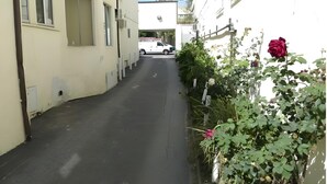 A narrow street with buildings on either side, a parked white vehicle, and a rose bush with a single rose. - Budget Inn Hollywood (Hollywood)