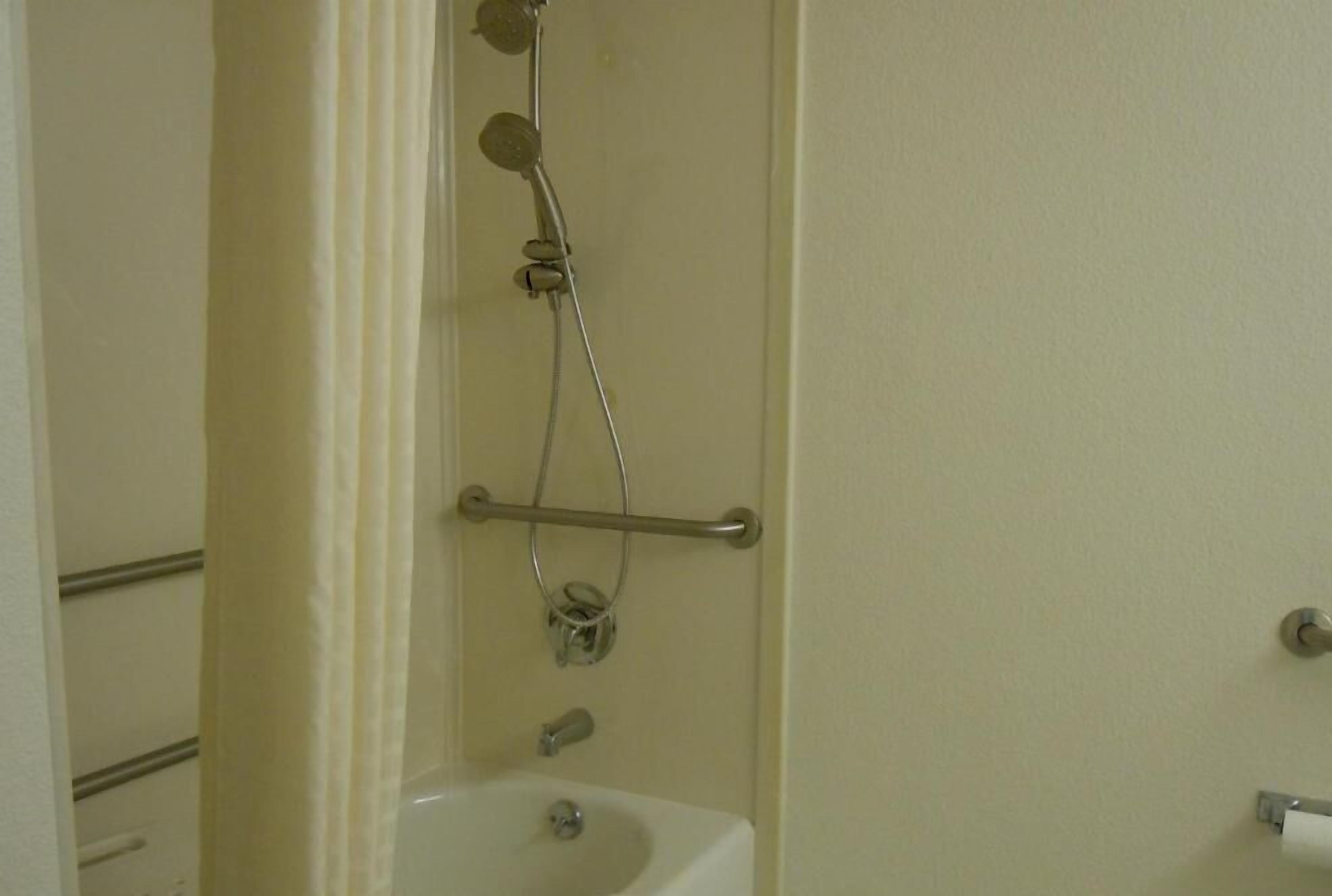 Un baño con lavamanos blanco, cabezal de ducha de mano y barra de apoyo.