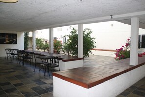 An outdoor patio area with a long wooden table and several chairs, surrounded by white pillars and potted plants. - Airport Inn (South San Francisco)