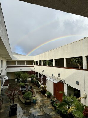 A spacious courtyard with a visible rainbow, potted plants, and a covered seating area. - Airport Inn (South San Francisco)